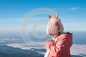 Cute asian child girl wearing sweater and warm hat making folded hands in prayer in beautiful mist and mountain background