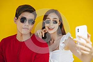 Cute asian couple taking selfie with smartphone over orange background