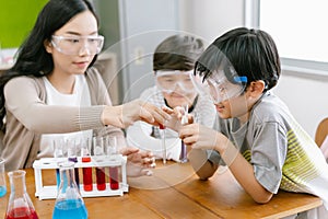 Cute Asian elementary schoolboy doing science while classmates looking his in science class with young Asian teacher. Child and