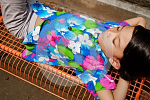 Cute Asian ethnicity little boy lying down on a bench enjoy sunbathing in the morning at home backyard