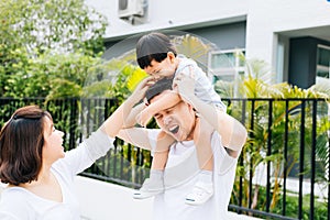 Cute Asian father piggbacking his son along with his wife in the park. Excited family spending time together with happiness.