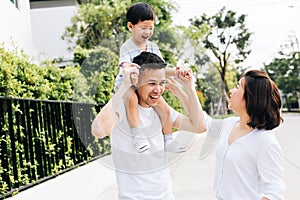 Cute Asian father piggybacking his son along with his wife in the park. Excited family spending time together with happiness.