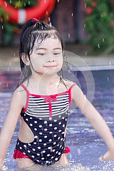 Cute asian female toddler child while playing and splashing water in a swimming pool