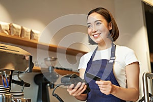 Cute asian girl, barista in cafe processing contactless payment, insert credit card into POS terminal, taking order in