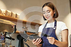 Cute asian girl, barista in cafe processing contactless payment, insert credit card into POS terminal, taking order in