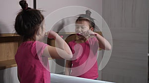 Cute asian girl brushing teeth at bathroom mirror