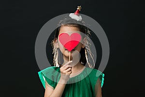 cute asian girl child dressed in a green dress holding a Christmas ornament and a heart stick on a black background