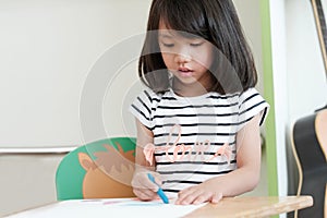 Cute asian girl drawing color pencils in kindergarten classroom, preschool and kid education concept