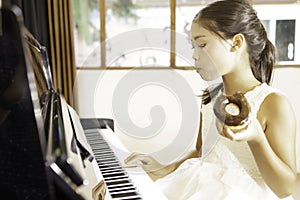 A cute Asian girl eating donuts while rehearsing the piano