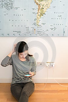 Cute asian girl frustrating with phone's battery, charging on the wall