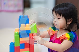 Cute Asian girl is having fun playing with colorful plastic blocks, an activity that enhances learning, enjoying a fun and photo