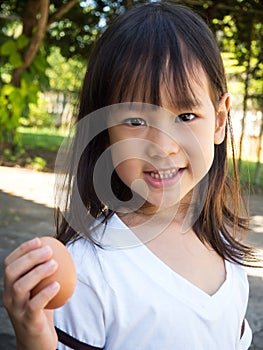 Cute Asian girl holding egg in hand. Showing egg and smiling. Co