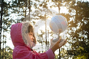 Cute Asian girl learning model of the world on nature background and warm sunlight in the park. Children learn through educational