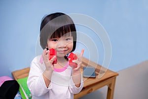 Cute Asian girl playing with orange-red square blocks wooden. Mobile phones placed on wooden tables. Light blue background.