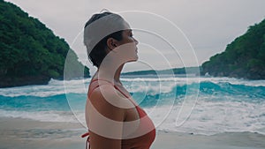 Cute Asian girl with short wet hair touching herself as she is enjoying peaceful moment of freedom and joy on wild beach