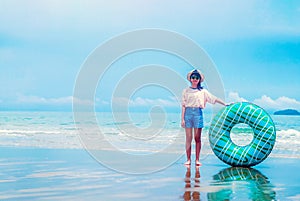 Cute asian girl on summer sea beach holding swim ring, wearing hat, eyeglasses and smiling with happiness, people on summer