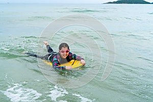 Cute asian girl wearing a black swimsuit running on the waveboard surf in the sea on a bright day