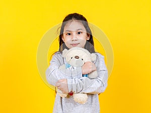 Cute Asian girl wearing sweater, taking portrait photo hugging lovely bear doll on yellow background