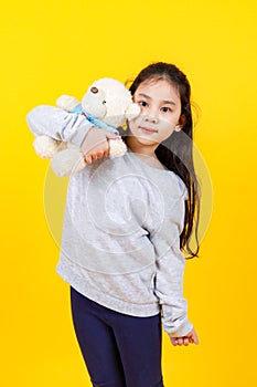 Cute Asian girl wearing sweater, taking portrait photo hugging lovely bear doll on yellow background