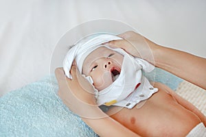 Cute asian infant baby boy lying on bed and mother while put on some clothes to her baby after bath