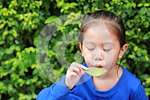 Cute Asian kid girl plays a melody by blowing air through the mouth with a leaf in the garden