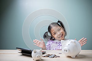The cute Asian kid girl is very happy saving money to spend in the future with a piggy bank, stack coins, and calculator.