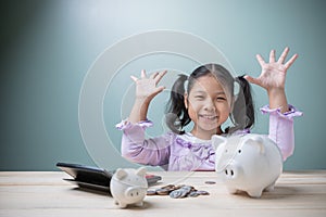 The cute Asian kid girl is very happy saving money to spend in the future with a piggy bank, stack coins, and calculator.