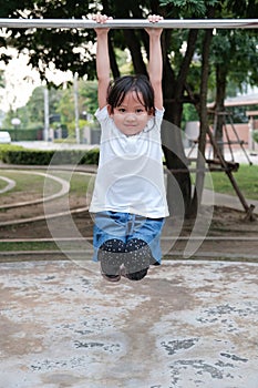 Cute Asian kid hanging on pull-up bar at playground in the village park. Sport outdoor activity for kid