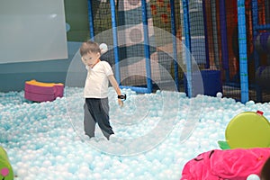 Cute Asian kid standing and throwing ball in ball pit full of plastic balls, Kindergarten boy having fun playing alone in children