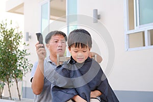Cute Asian kid young boy getting a haircut at home backyard, Father makes a haircut for his son