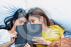 Cute Asian lesbian couple reading book together and lying on bed. Lifestyles and lovers concept. Happiness life and relax theme