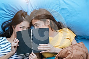 Cute Asian lesbian couple reading book together and lying on bed. Lifestyles and lovers concept. Happiness life and relax theme