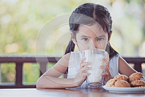 Cute asian little child girl is drinking a milk from glass