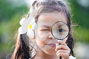 Cute asian little child girl looking through a magnifying glass