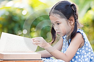 Cute asian little child girl reading a book in outside