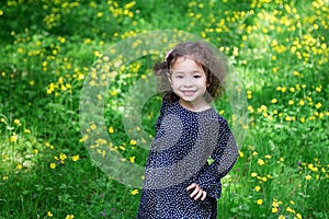 Cute asian little girl in black dress with white flowers and curly hair is enjoying sunny day in the park.