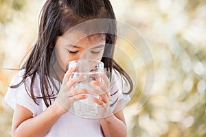 Cute asian little girl drinking fresh water from glass photo