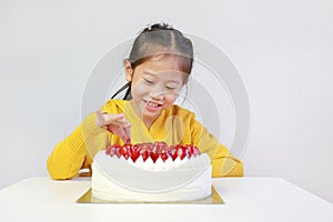 Cute asian little girl eating strawberry cake. Kid picking strawberries top of cake