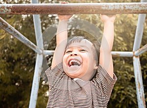 Cute Asian little girl hanging the monkey bars by her hand to exercise at out door playground on sunny day