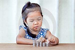 Cute asian little girl playing with coins making stacks of money