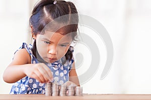 Cute asian little girl playing with coins making stacks of money