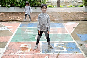 Cute Asian little girl playing hopscotch outdoor. Funny activity game for kids on the playground outside. Summer backyard street