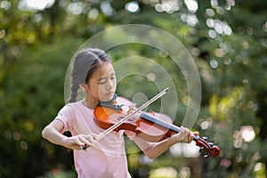 Cute Asian little girl playing the violin in the park