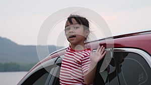 Cute asian little girl smiling and having fun to travel by car and looking out of the car window. Happy family enjoying road trip