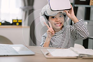 Cute Asian little girl wearing VR glasses with a laptop placed on the table in STEM technology class. Online education. Erudition photo