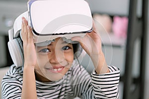 Cute Asian little girl wearing VR glasses with a laptop placed on the table in STEM technology class. Online education. Erudition