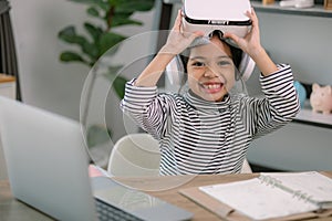 Cute Asian little girl wearing VR glasses with a laptop placed on the table in STEM technology class. Online education. Erudition