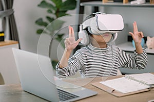 Cute Asian little girl wearing VR glasses with a laptop placed on the table in STEM technology class. Online education. Erudition