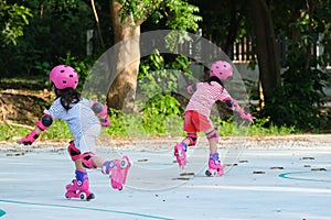 Cute Asian little girls in protective pads and safety helmet practicing roller skating in the park. Exciting outdoor activities