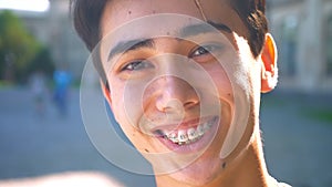 Cute asian man close-up smiling in braces and looking at camera relaxed, chill mood, outside, sunshines